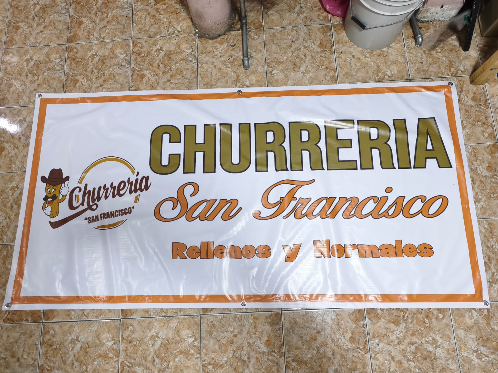 Lona impresa a todo color de una churrería con borde naranja y ojillos metálicos